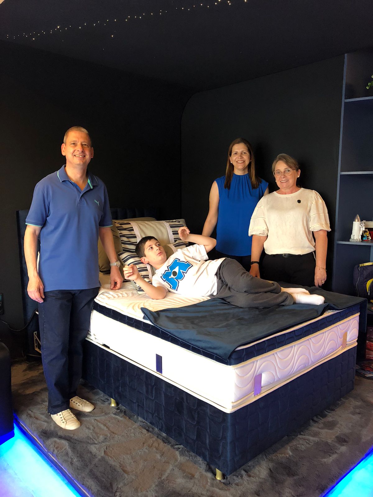Suíte Matheus na CasaCor 2021: cabeceira azul, iluminação de teto pontual e cama adaptada para acolhimento.